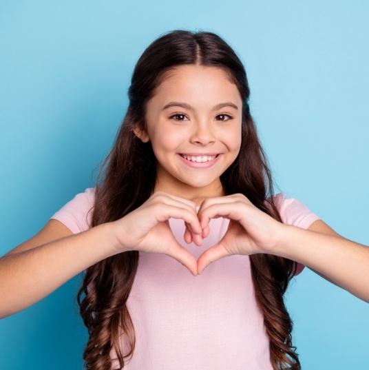 Little girl in pink shirt making heart shape with her hands
