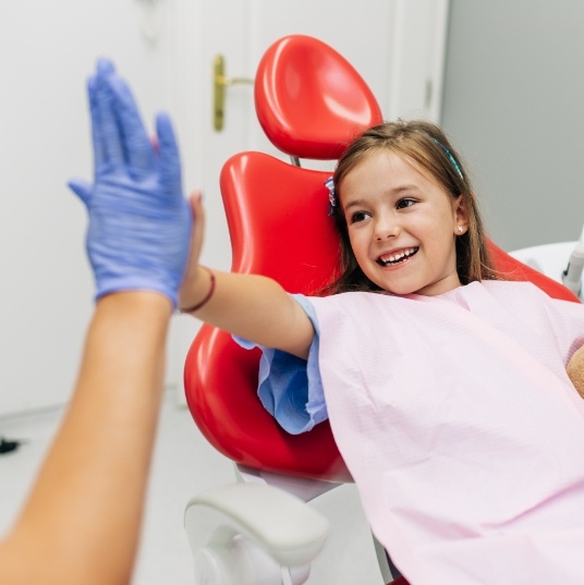 Young girl in dental chair giving high five to dental team member