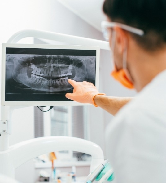 Dentist pointing to a set of dental x rays on a screen