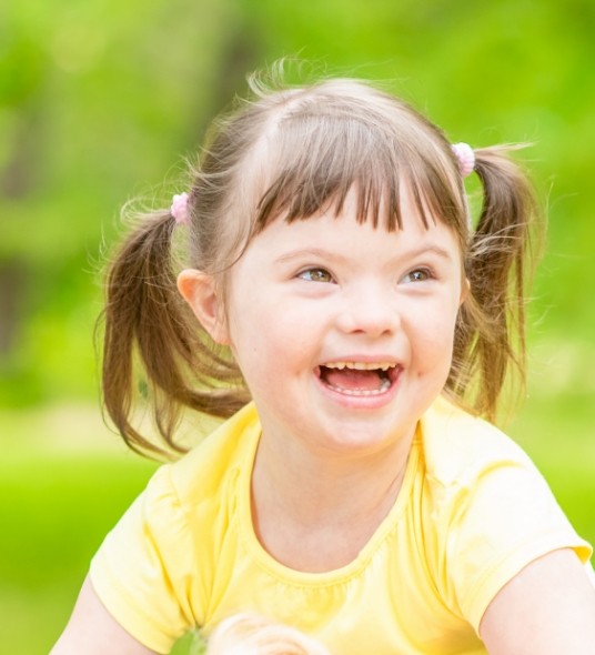 Young girl with special needs grinning outdoors on sunny day
