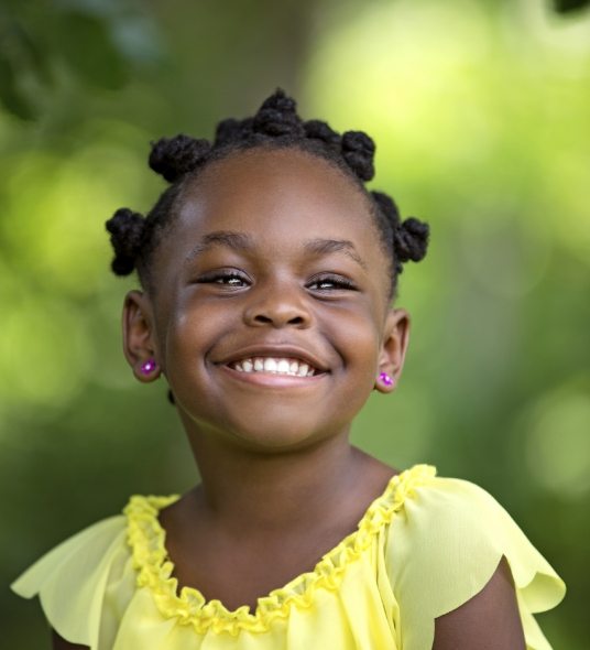 Young girl in yellow blouse smiling after pediatric restorative dentistry in Independence
