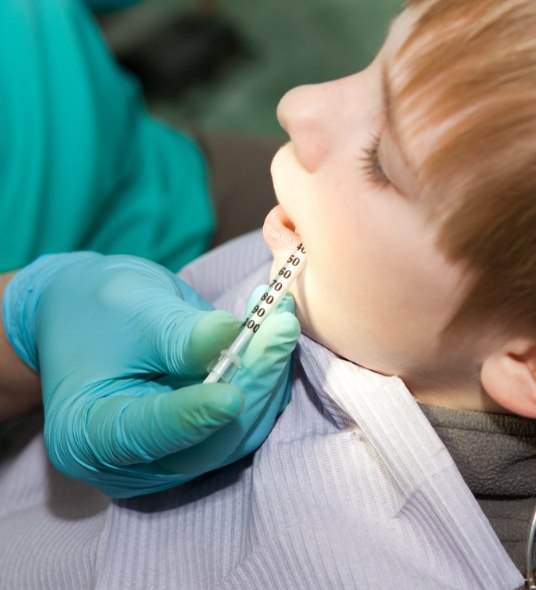 Dental team member placing a syringe in a child patient's mouth